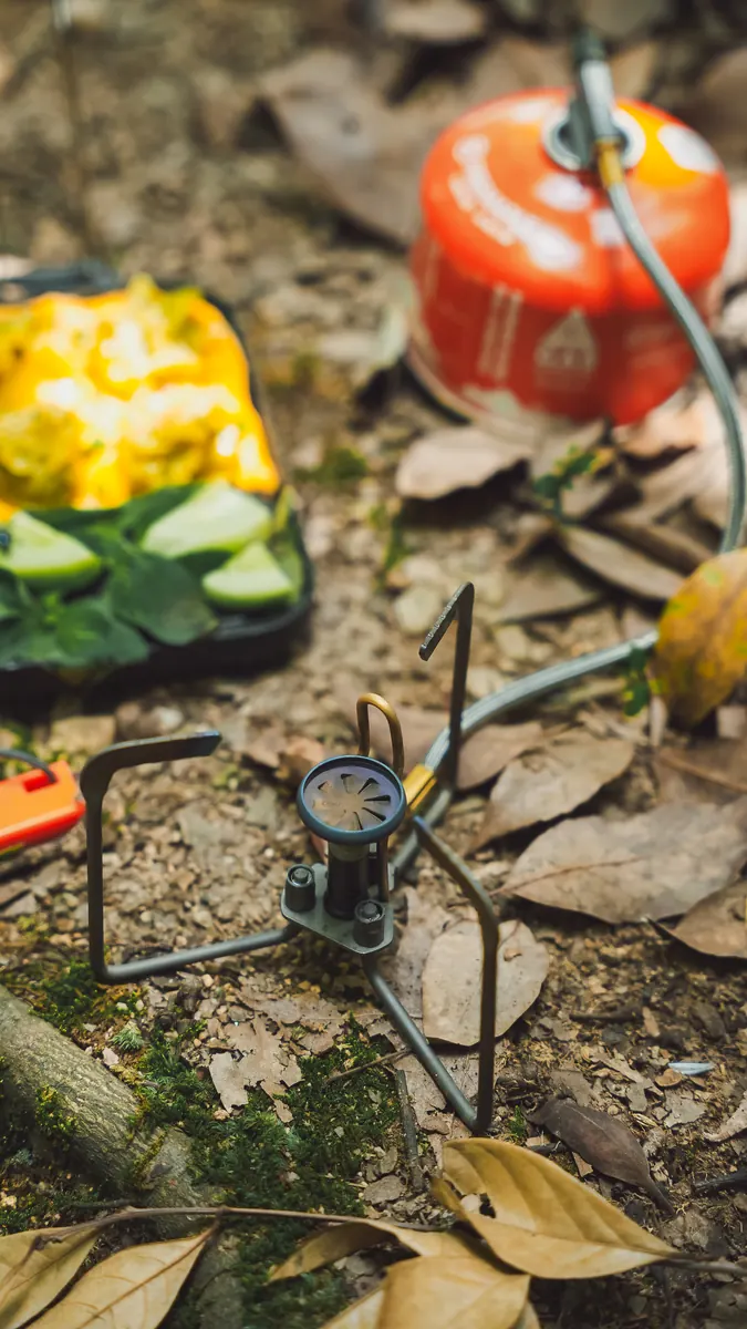 The Petrel Summit stove set up on a forest floor beside a gas canister and a plate of cooked food.
