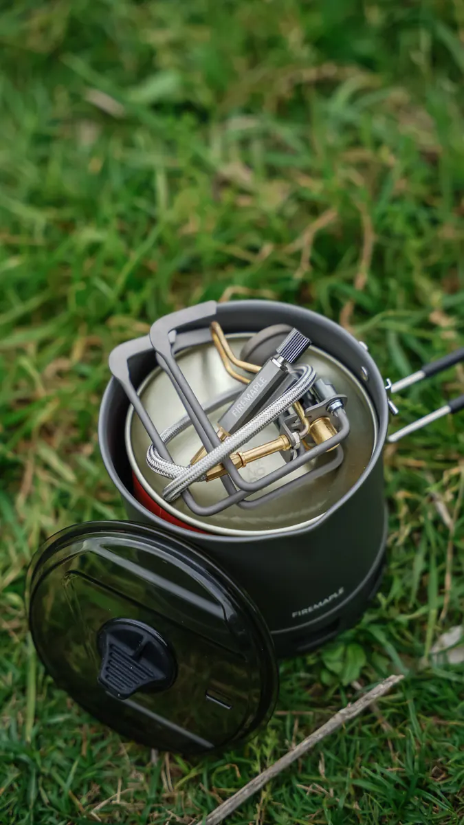 The Petrel Summit stove packed inside a Fire Maple cook pot on grass, with the pot lid alongside.