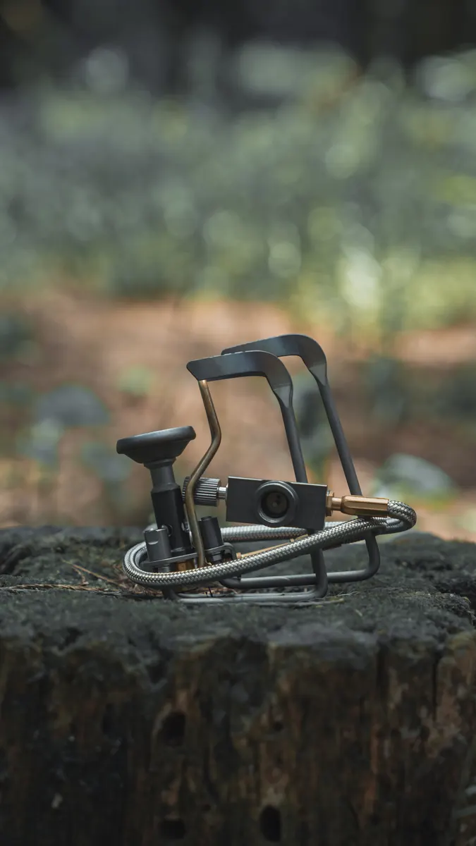 The Petrel Summit stove standing on a tree stump in woodland, its pot supports folded out and its fuel hose coiled beside it.